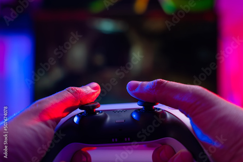 Close-up. Joystick in the hands of a gamer on a dark background. Neon lighting. Video games on modern digital equipment. Cyberspace, cybersport, virtual reality.