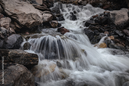 Close-up shot of a mountain stream with a waterfall runs over the stones between the rocky banks © Igor