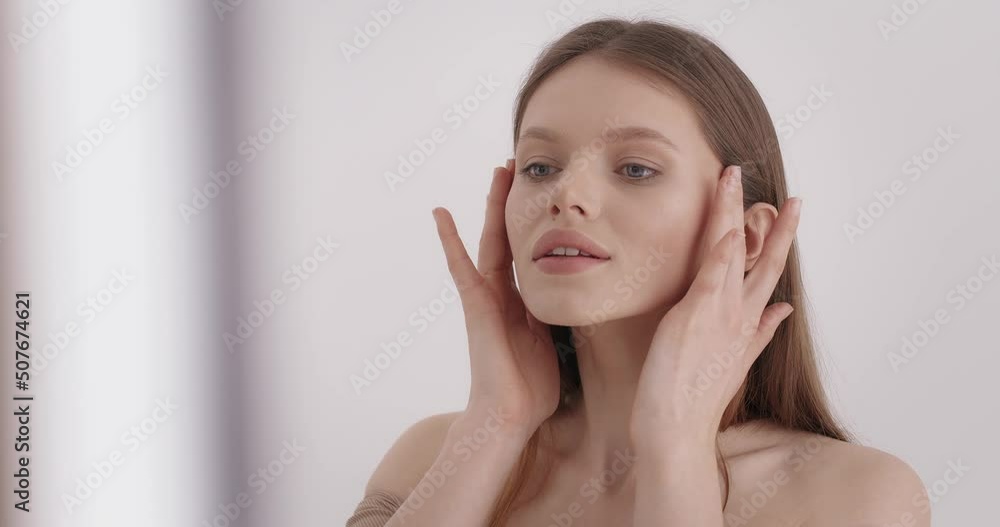Skin care. Attractive caucasian woman with bare shoulders gently touching her smooth shiny face