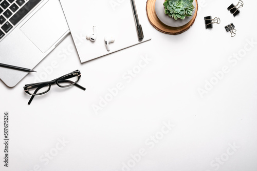 Top view above of white office desk table with keyboard, notebook and pen, glasses, headphones, succulent and other office supplies. Workplace, Flat lay, copy space. Concept business and finance. photo