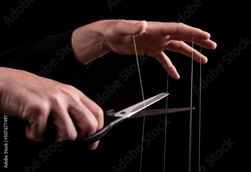 Overcoming addiction. Man cutting strings on fingers with scissors. Freedom, liberation from slavery, abuse, manipulation concept. Getting rid of bad habits. High quality photo