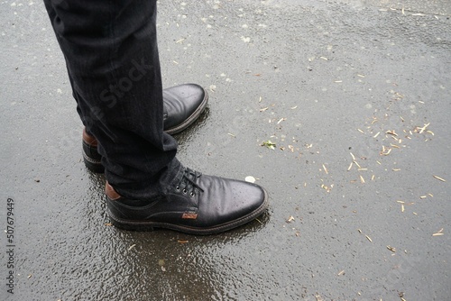 Schwarzes Paar Lederschuhe mit schwarzen Hosenbeinen von Mann auf nasser Straße bei Regen im Frühling  © Anette