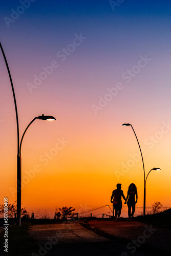 Silhueta de um casal de namorados andando de mãos dadas em direção ao por do sol em final de tarde © Eduardo