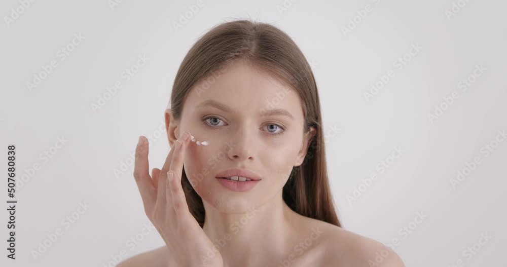 Beauty skin care. Portrait of adorable young woman applying face cream with finger over grey studio background. Charming caucasian blonde using professional cosmetic for moisturizing. Beauty skin care. Portrait of adorable young woman applying face cream with finger over grey studio background. Charming caucasian blonde using professional cosmetic for moisturizing.