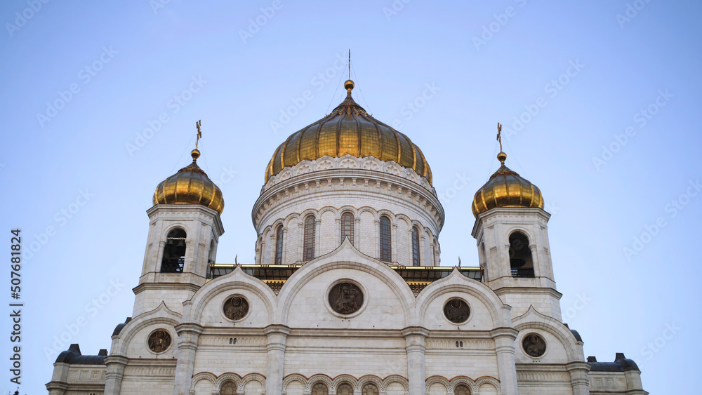 Beautiful facade of white temple on background blue sky. Action. Bottom view of ancient architecture of Russian white temple with Golden domes. Historical Orthodox churches in Russia
