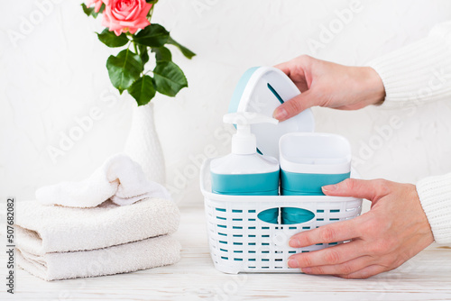 Women s hands put bathroom accessories in a basket and a stack of towels on the table