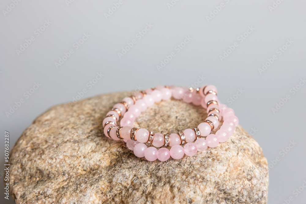 Two bracelets made of natural pink quartz stones beads isolated on pastel beige background. Handmade jewelry. Woman exoteric accessories. Talismans and amulets. Selective focus - obrazy, fototapety, plakaty 