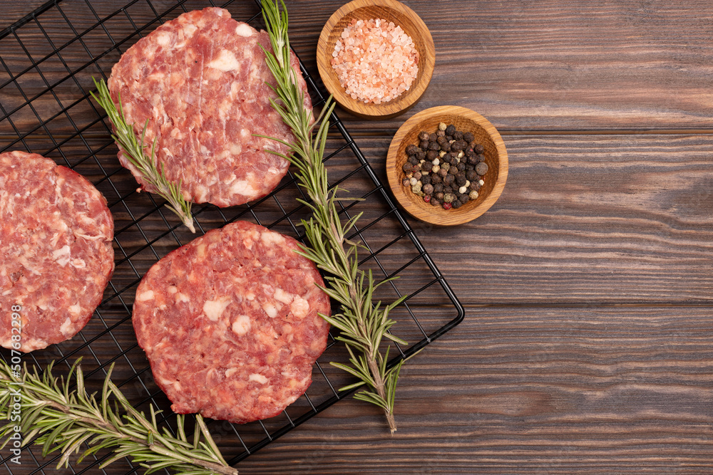 Homemade minced pork and beef patties, with spices, rosemary, ready for roasting, for cooking burgers on a grill, on a wooden background, flat lay, open space