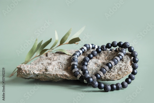 Two bracelets made of natural black volcanic lava stones beads isolated on pastel greenbackground. Handmade jewelry. Woman exoteric accessories. Talismans and amulets. Selective focus photo