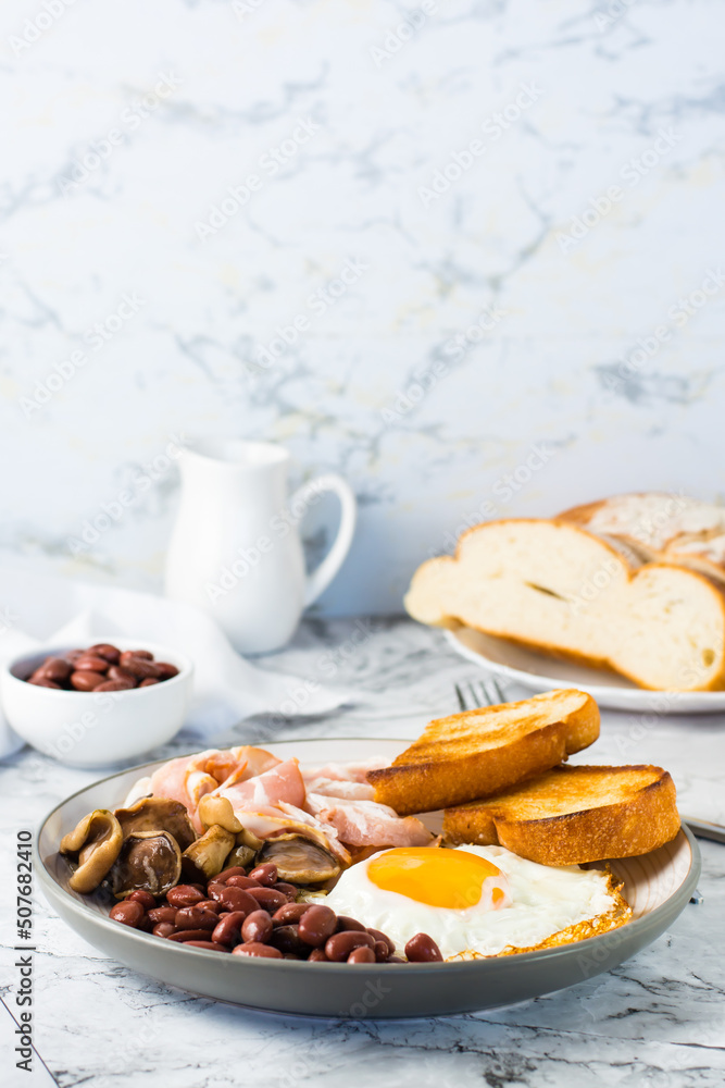 Traditional English breakfast with egg, bacon, beans, mushrooms and toast on a plate. Vertical view