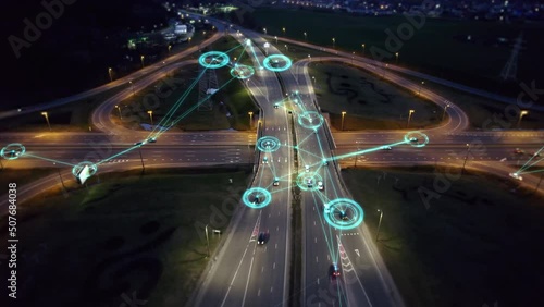 Self-driving autonomous cars move along a suburban traffic intersection in the evening. Neon HUD elements visualize the interaction of driverless cars connected to a common network and controlled remo photo