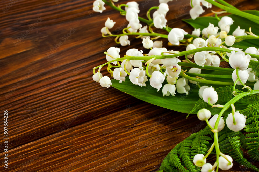 Bunch of natural green fern leaves with lily of the valley or may bells flowers on a wooden background. Copy space. Top view. Bunch of natural green fern leaves with lily of the valley or may bells flowers on a wooden background. Copy space. Top view.
