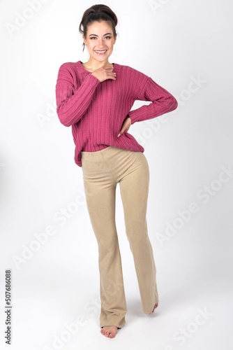 Beauty, fashion and makeup concept. Beautiful long hair brunette woman portrait with purple sweater and beige tight trousers. Studio shot with copy space. Model with bare feet. Model looking to camera © Rytis