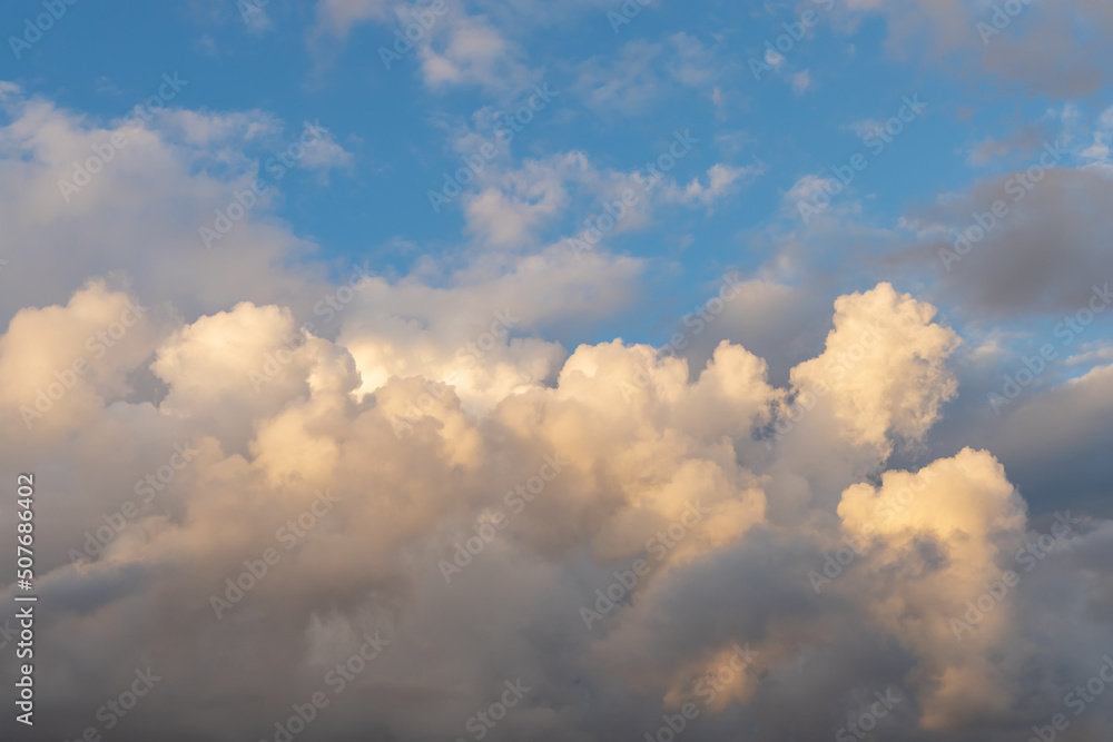 Cumulonimbus clouds against the blue sky. Picturesque cumulus clouds in the yellow light of the setting sun. Dramatic sky