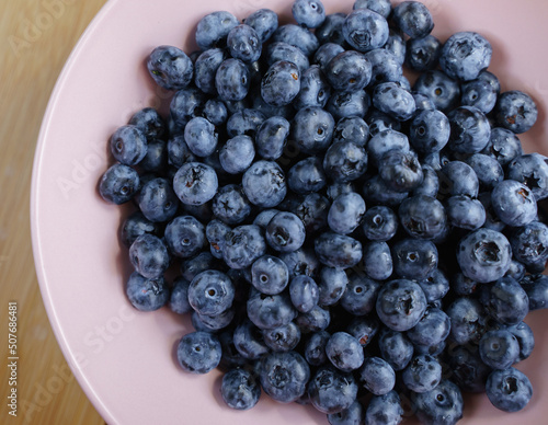 Delicious ripe blueberries in a pink plate on a wooden table.