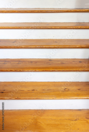 Vintage wooden stair with brown plank tread and white riser. Wood shelf on white painted wall.