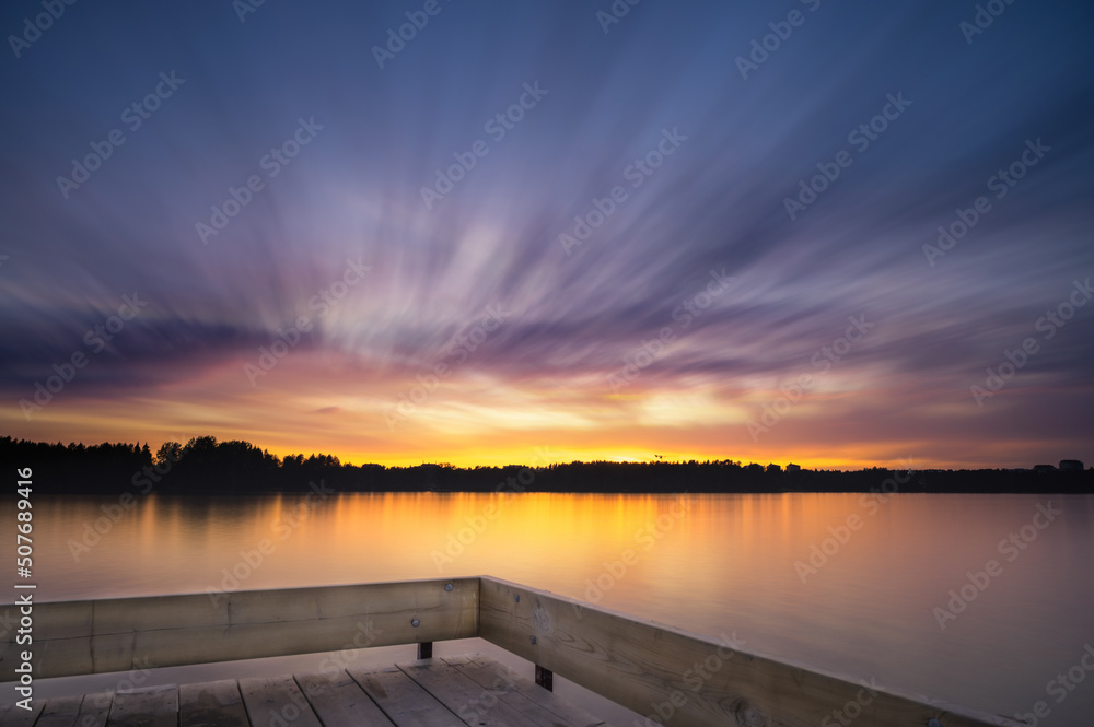 Panoramic Tranquil golden hour cloud above the forest lake at sunset. Dramatic cloudscape. Long exposure on the water