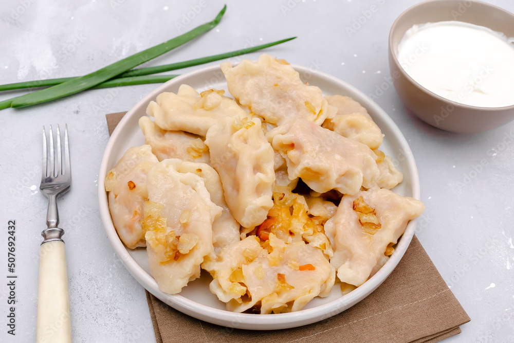 Homemade dumplings, vareniki, varenyky, pyrohy with stewed cabbage fried with onion on plate.Traditional ukrainian popular national dish,cuisine served with sour cream on gray background Homemade dumplings, vareniki, varenyky, pyrohy with stewed cabbage fried with onion on plate.Traditional ukrainian popular national dish,cuisine served with sour cream on gray background
