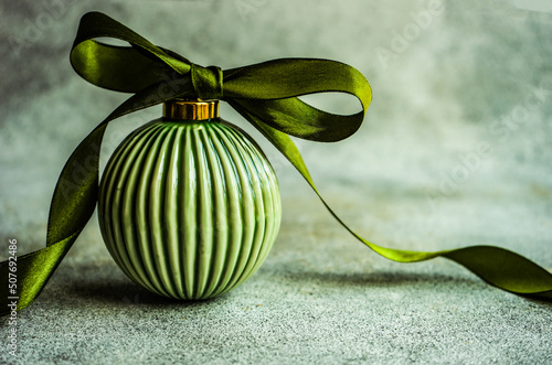 Close-up of an elegant green ceramic Christmas bauble with a tied ribbon bow on a table photo