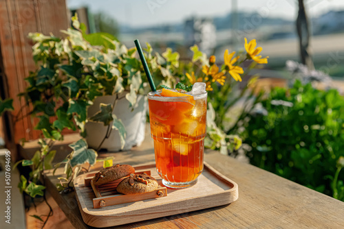 Fresh homemade peach ice tea with mint, chocolate chip cookie served on table outdoors. summer cold fruit drink in sunny afternoon with yellow flowers behind