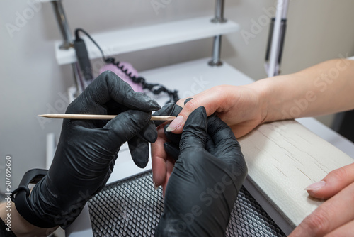 Nail salon.Professional beautician cleaning client's nails with orange stick, cuticle pusher, cuticle removal in beauty salon.