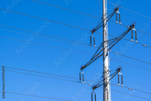 Galvanized metal pole with high-voltage electrical wires, blue clear sky in the background.