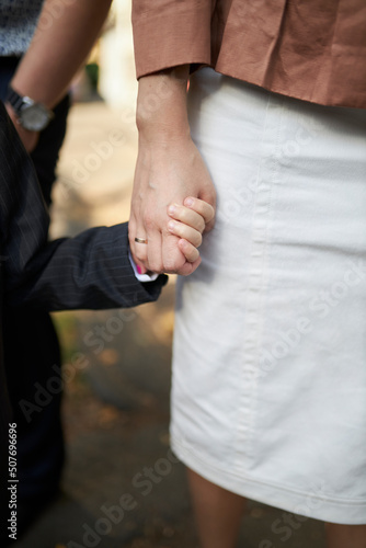 mom holding her son's hand in the park, close-up of hands, blurred background