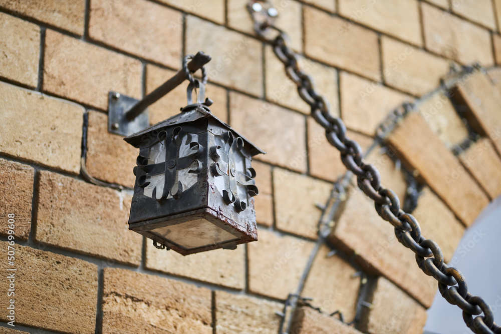 Metal lamp on a brick background. Ancient lamp on the wall of the castle Metal lamp on a brick background. Ancient lamp on the wall of the castle