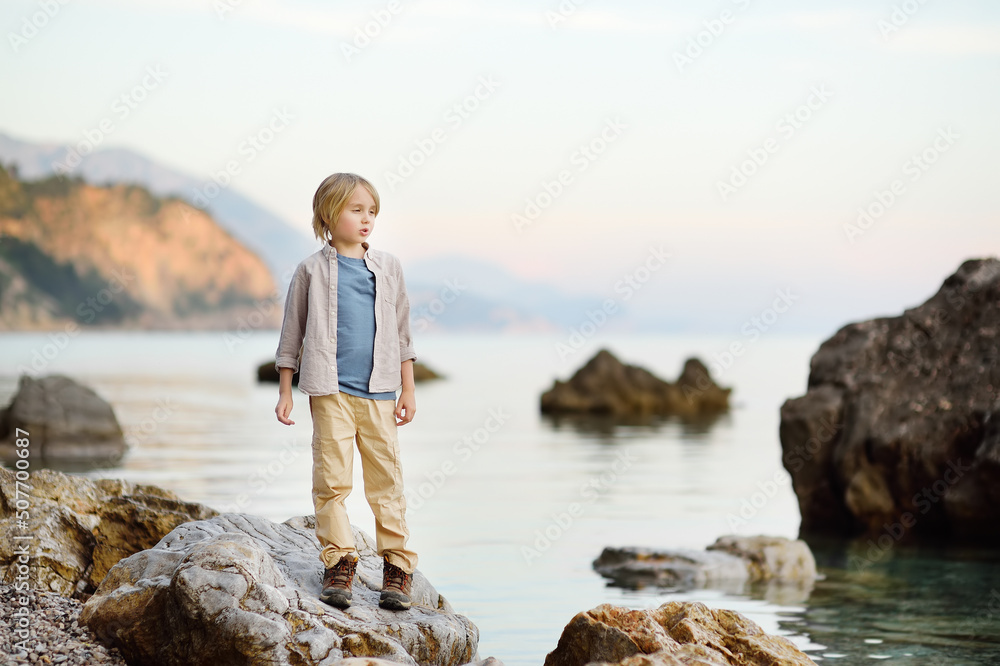 Cute schoolchild hiking by rocks near sea, having fun and exploring nature.