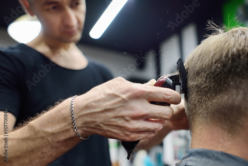 Hairdresser is cutting hair of handsome bearded mature man in salon. Stylist making hairstyle with electric shaver for person in barbershop. Services of a professional stylist. Fashion haircut © Maria Sbytova