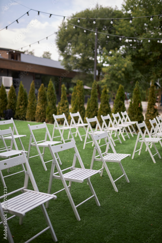 White folding chairs stand in rows in the meadow. beautiful white chairs 
