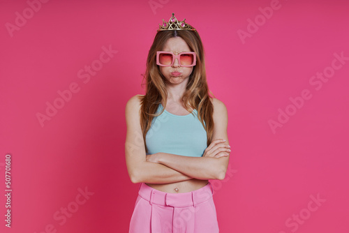 Displeased woman in funky crown showing her thumb down while standing against pink background © gstockstudio