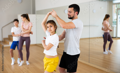 Young adult man practicing dance in pair with his tween daughter during family dance class