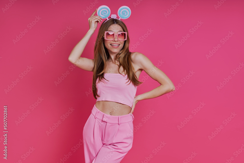 Happy young woman in party headwear smiling while standing against pink background Happy young woman in party headwear smiling while standing against pink background