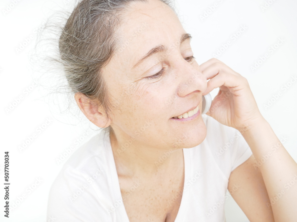Forty nine year old woman in a white T-Shirt against a white background talking on her cellphone Forty nine year old woman in a white T-Shirt against a white background talking on her cellphone