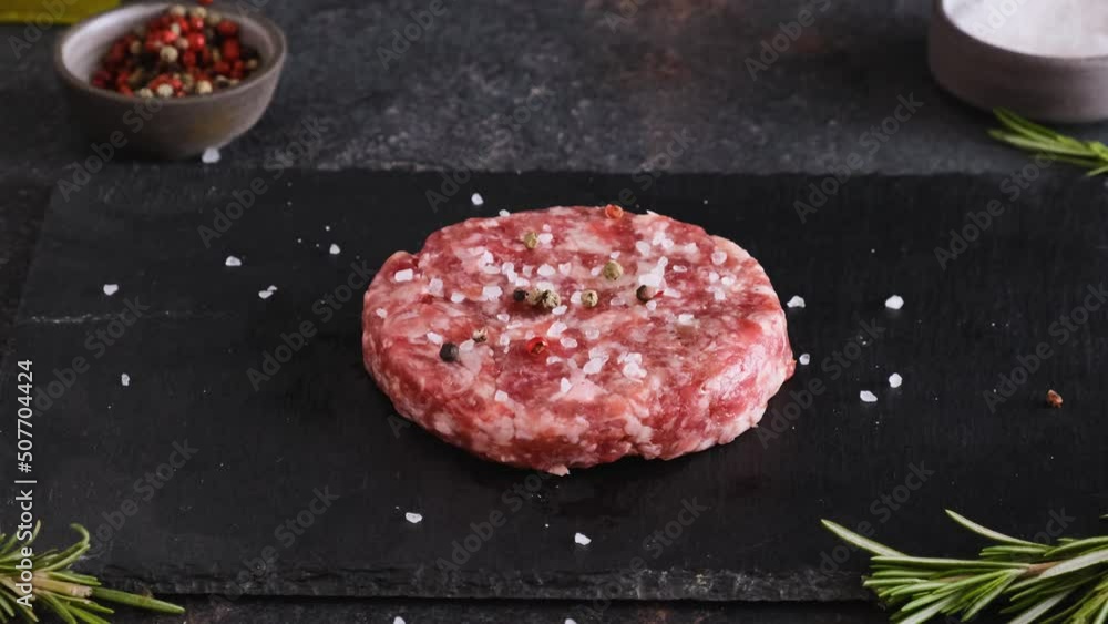 Strewing pepper on raw beef burger patty on dark background. Cooking concept. 4k video Strewing pepper on raw beef burger patty on dark background. Cooking concept. 4k video