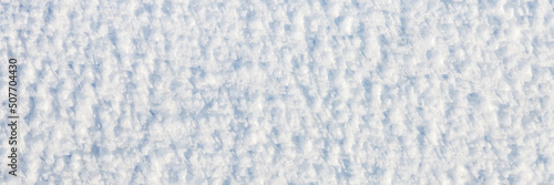 Natural snow texture. The surface of an icy snow crust. Snowy ground. Winter background with snow patterns. Closeup top view. Wide panoramic texture for background and design.