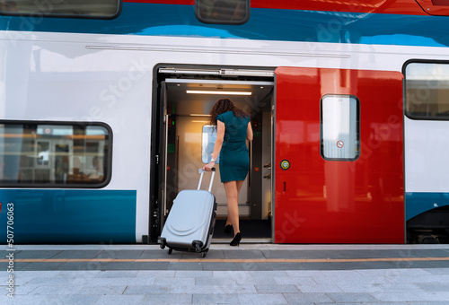 Young woman entering modern electric train with luggage 