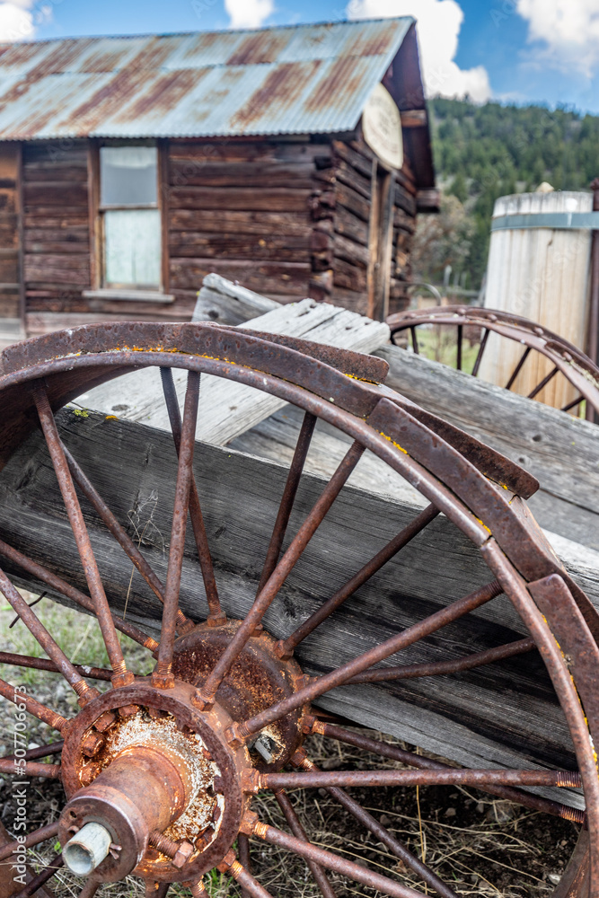 Old rusty wheel on cart with log cabin in background