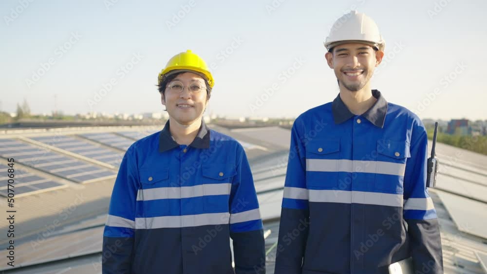 Portrait of two Asian engineer on background field of photovoltaic solar panels solar cells on roof top factory.