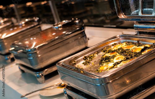 Breakfast buffet food in heating trays in hotel restaurant with eggs with spinach