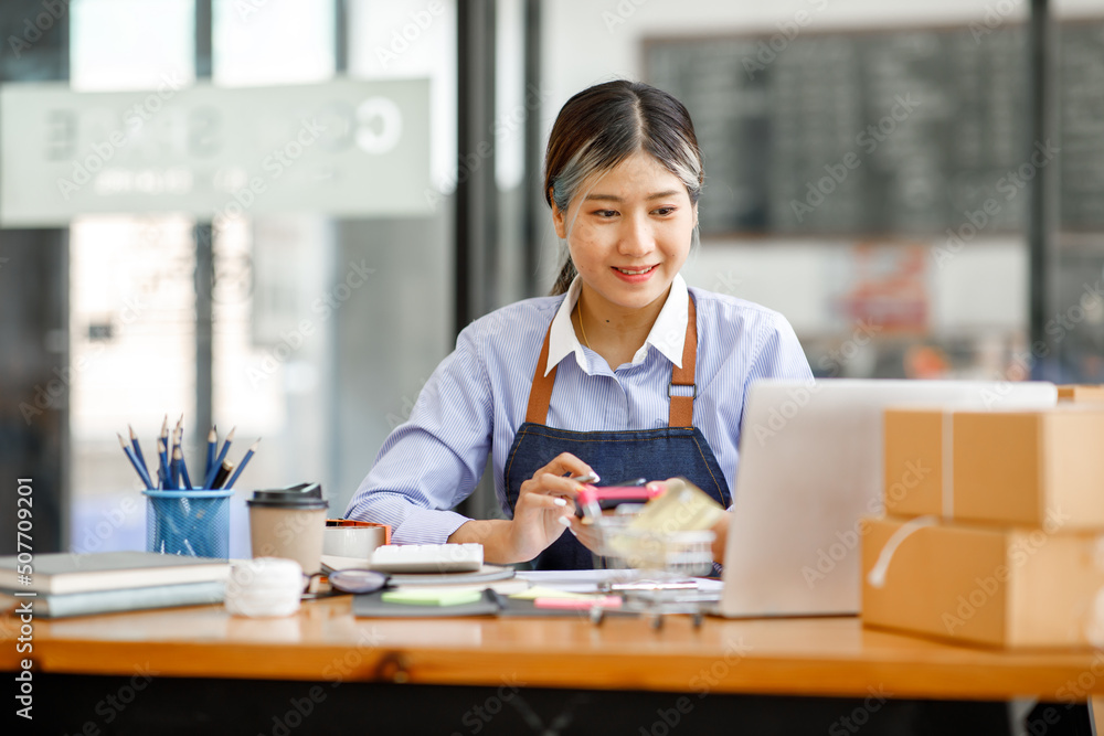 Young Asian entrepreneur SME woman checking product on stock take note with a laptop. Small business owner working at home. Check address on the parcel SME online start up freelance concept. Young Asian entrepreneur SME woman checking product on stock take note with a laptop. Small business owner working at home. Check address on the parcel SME online start up freelance concept.