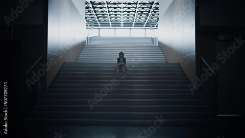 Lonely schoolchild sitting alone on school staircase closeup. Boy hide in hall.