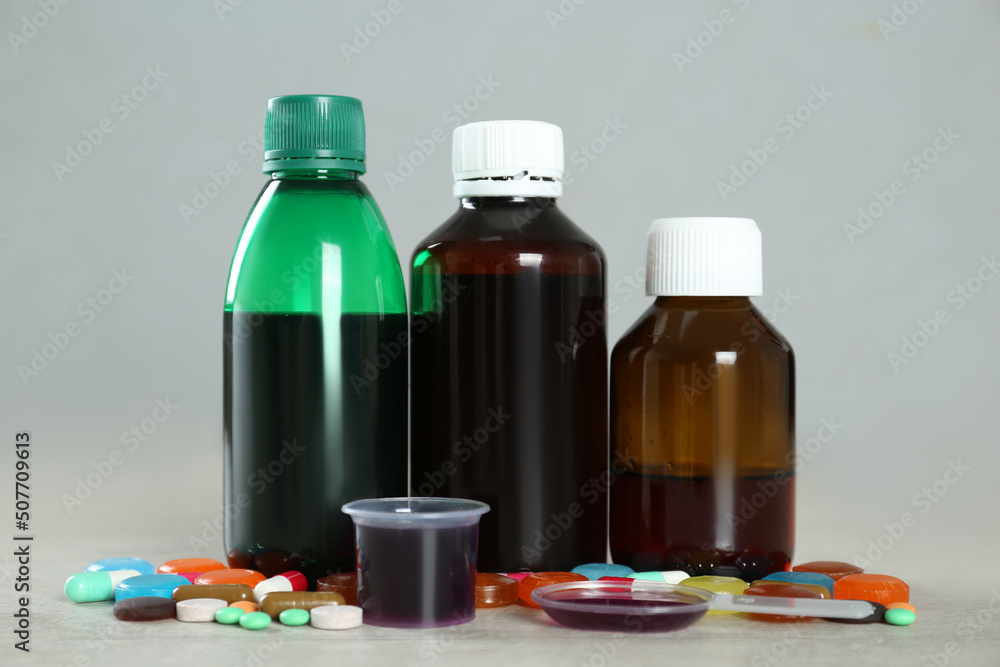 Bottles of cough syrup, dosing spoon, measuring cup and pills on light background Bottles of cough syrup, dosing spoon, measuring cup and pills on light background