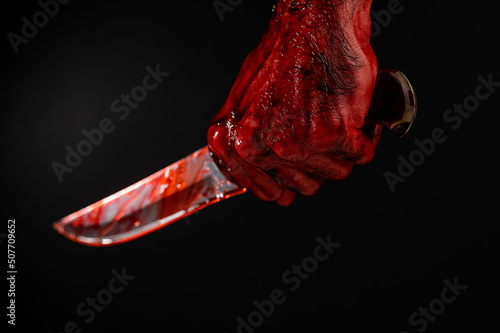 A man with bloody hands brandishes a knife on a black background.  photo