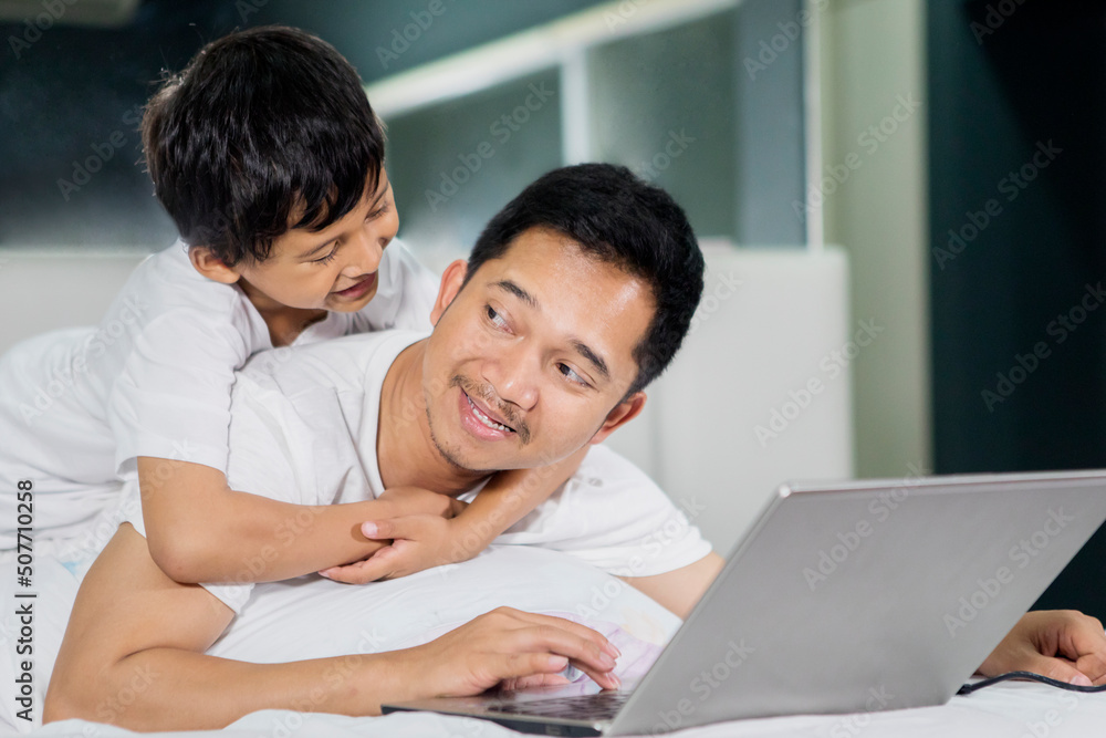 Little boy embracing his father while using laptop