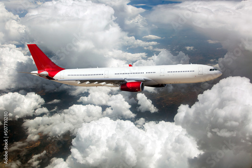 White passenger plane with red Tail in flight. The plane is flying over the clouds.