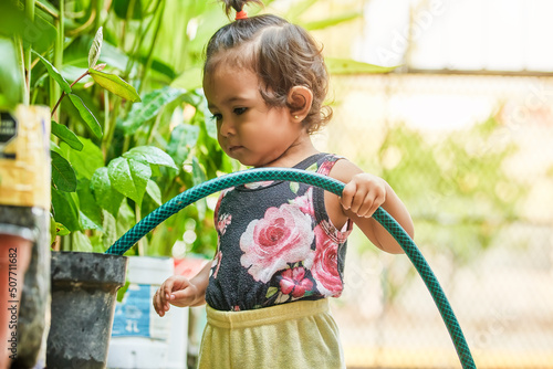 little latin girl taking care of the flora. girl watering the plants in her garden. Girl playing with water. photo