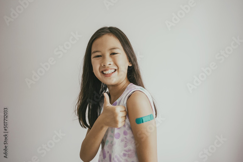 Foto Mixed Asian preteen girl showing her arm with bandage after got vaccinated or in