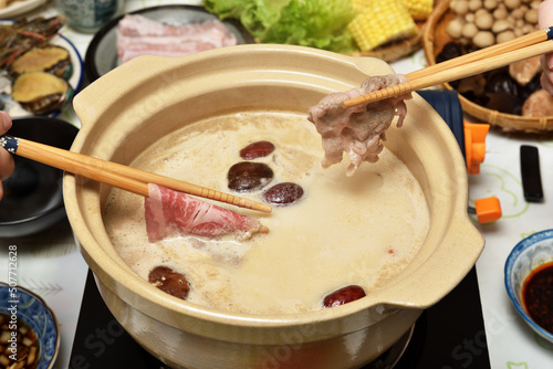 Two people use chopsticks to take meat slices from a hot pot